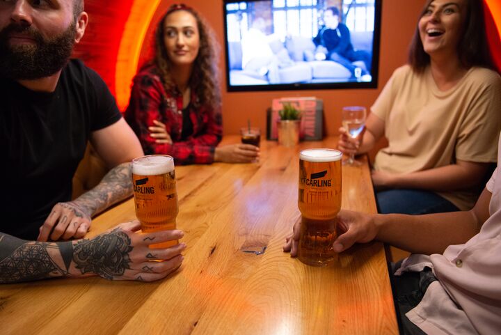 four people sitting around a table, holding carling beer pints